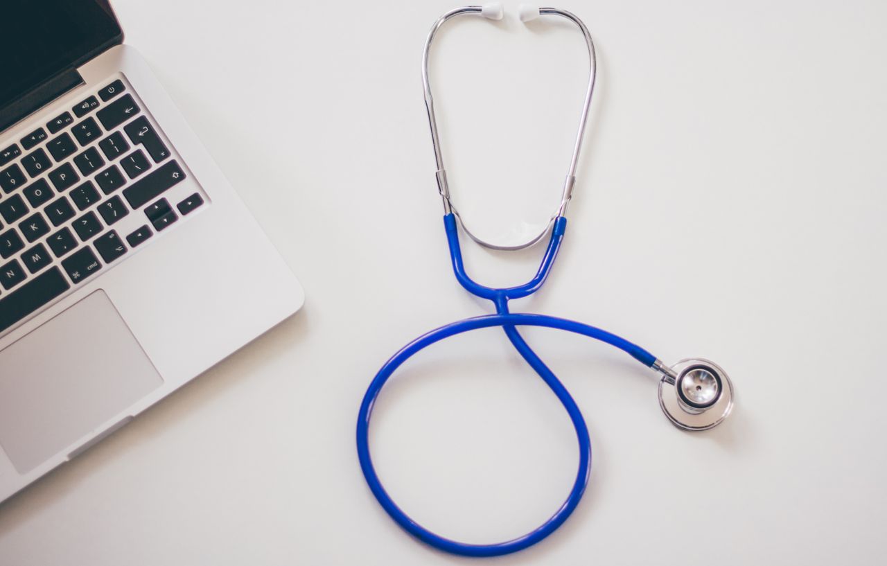 hero-img-02 Medical stethoscope and laptop on a white desk, symbolizing digital health solutions.
